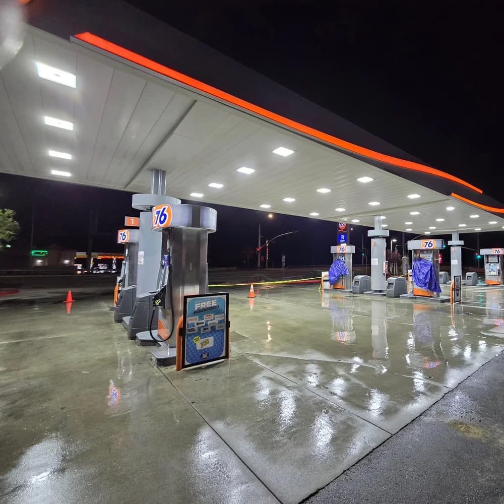 Night view of a 76 gas station with illuminated pumps and wet pavement.