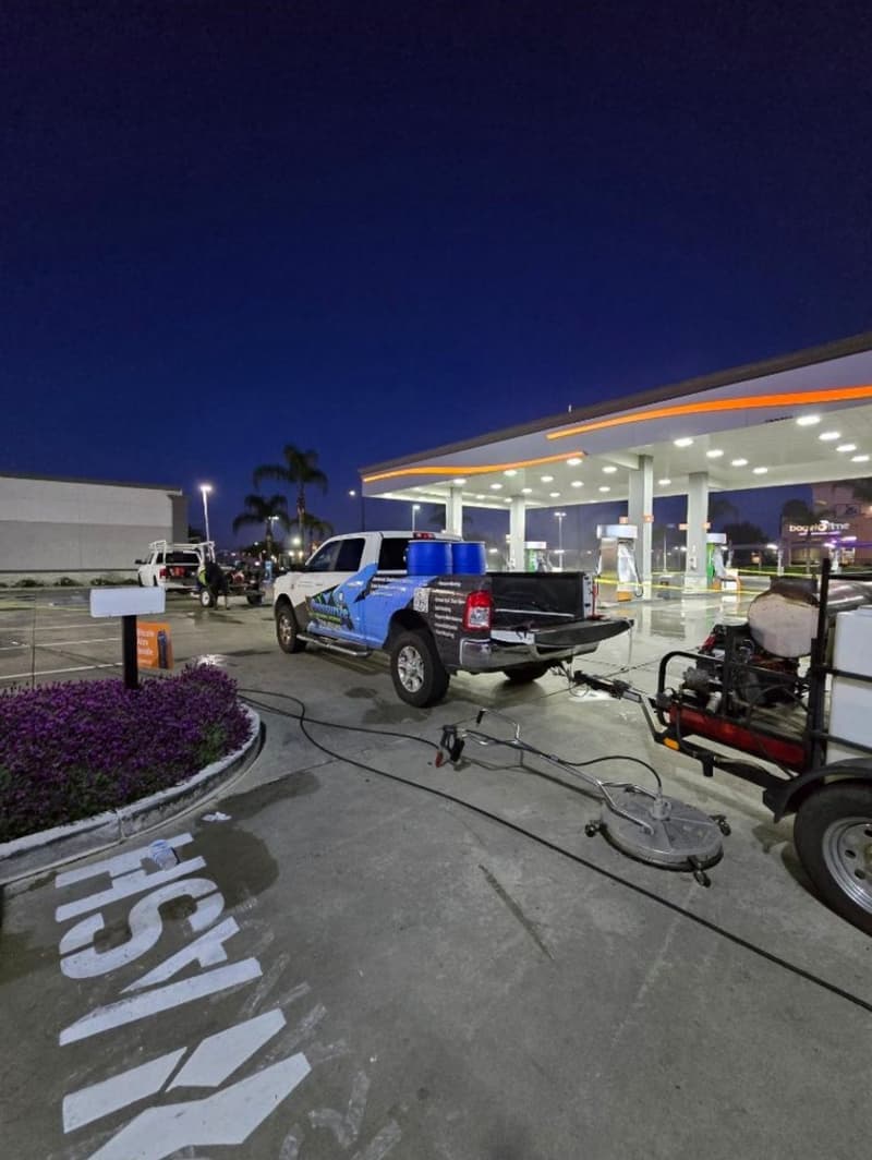 Truck with cleaning equipment at a gas station during twilight hours, palm trees in background.