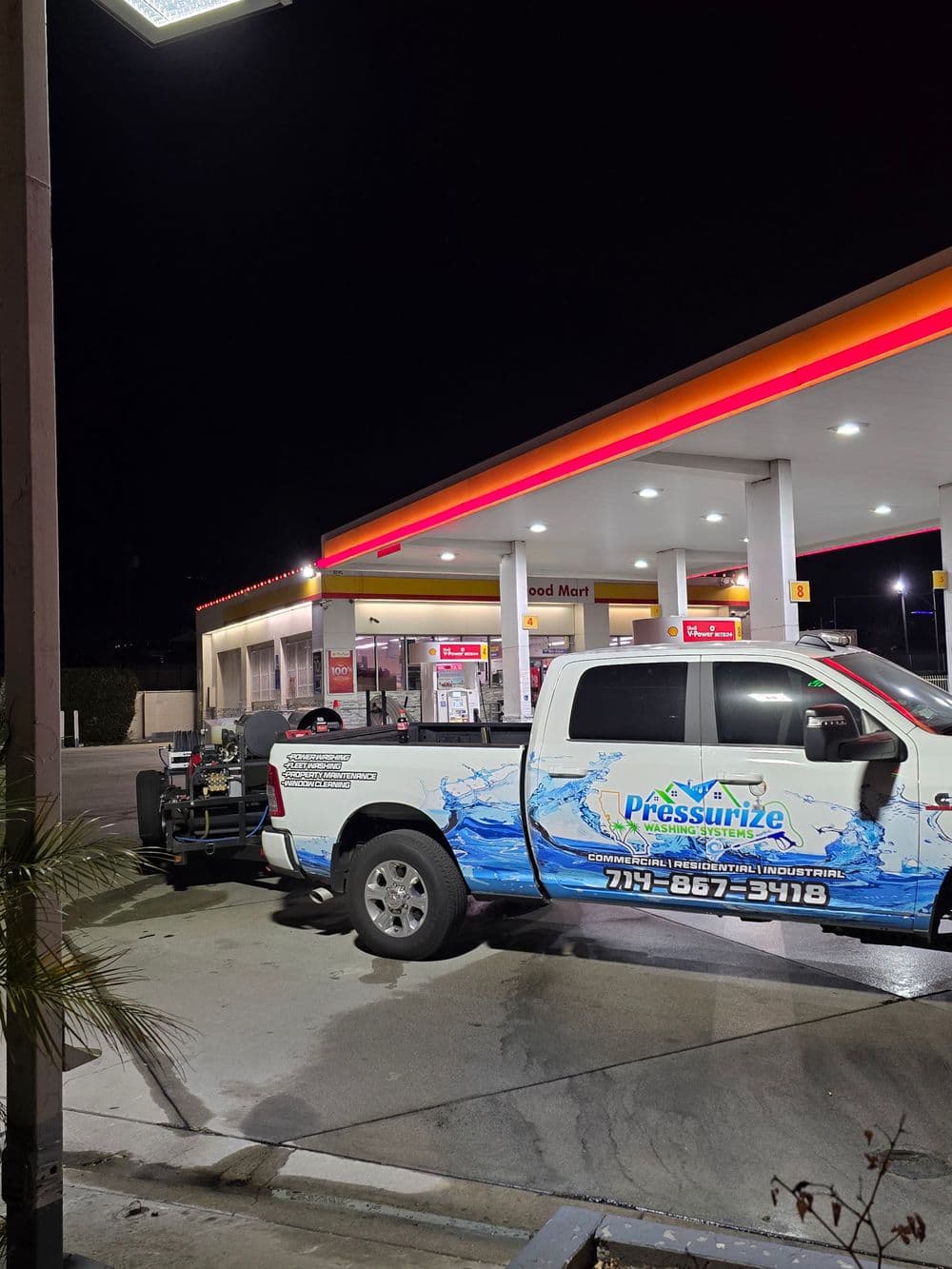 Pressurize truck parked at a gas station at night with bright signage and storefront visible.
